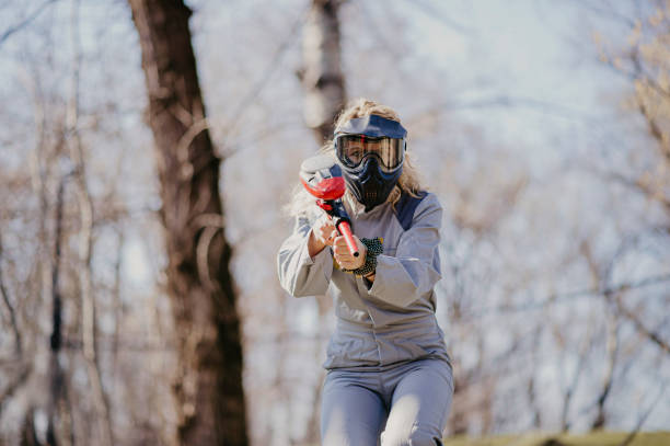 Paintball game, team in camouflage protective uniform with paintball guns and ammunition, strikeball arena battlefield, paintballer aiming and shooting at opponents, airsoft players match tournament