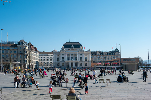 Zurich city Opera House. Wide angle view, daytime, blue sky. People sitting on public seats and benches enjoy early spring weather in the large square in front of the building.