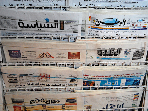 Picture of a press kiosk in the center of Vienna, Austria, filled with newspapers aligned in a magazine rack, all in German language.