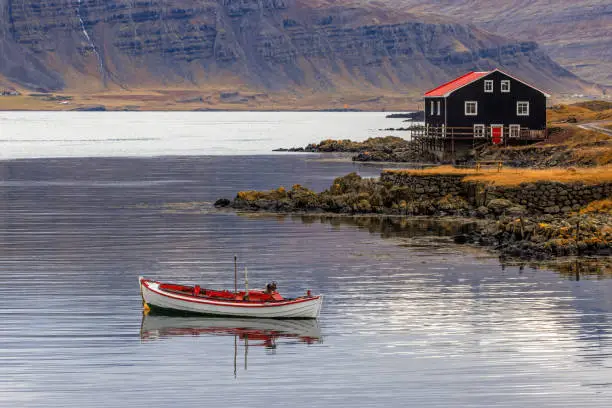 Photo of Small boat and black wooden house, Djupivogur, Eastfjords, Iceland. Landscape shot in autumn with mountain background.