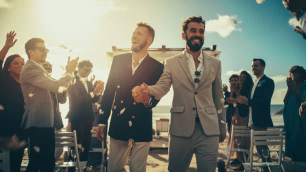 海の近くの屋外結婚式場で通路を歩くハンサムなゲイカップル。恋をしている二人の幸せな男が、多様な多民族の友人と彼らの大きな一日を共有しています。本格的なlgbtq関係の目標。 - homosexual wedding married engagement ストックフォトと画像