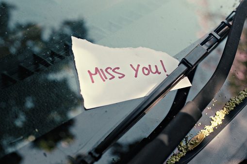 Notes placed under windshield wiper of car with the words Miss you