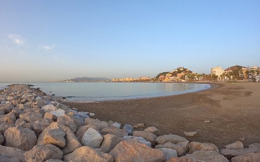 Seascape with Malaga and sunrise sunlight. Sandy beach of the Mediterranean Sea and walking stone pier in Playa de la Caleta, Spain, Europe