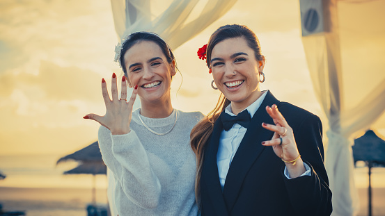 Portrait of a Happy Just Married Beautiful Lesbian Couple Kissing, Showing Off Their Gold Wedding Rings. Two Attractive Queer Women Smile and Pose for Camera. LGBTQ Relationship and Family Goals.