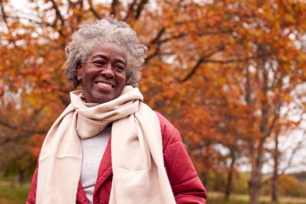 retrato de cabeza y hombros de una mujer mayor en un paseo por el campo otoñal contra hojas doradas - senior adult fotografías e imágenes de stock