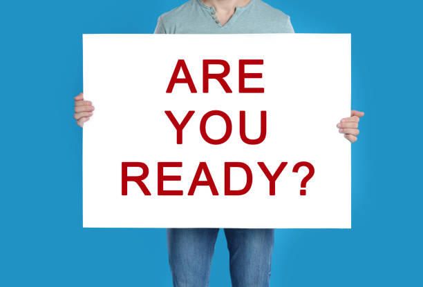 istock Man holding poster with text Are You Ready? on blue background, closeup 1388967443