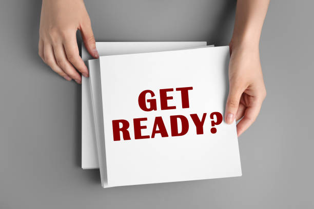 istock Woman holding paper sheet with text Get Ready? at grey table, top view 1388967456