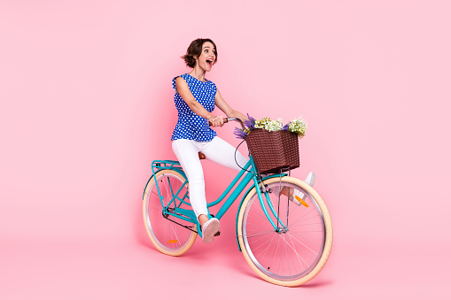 Full length photo of impressed millennial brunette lady ride bicycle wear blouse pants shoes isolated on pink background.