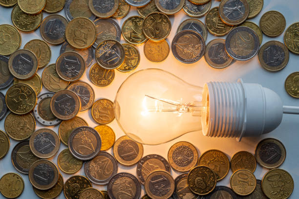 istock Light bulb turned on, with coins around. Energy costs. 1388967882