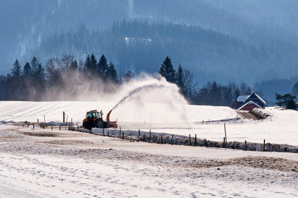 Captured on sunny March day, snow blower attached to tractor was expanding local roads covered by heavy snow fall.
