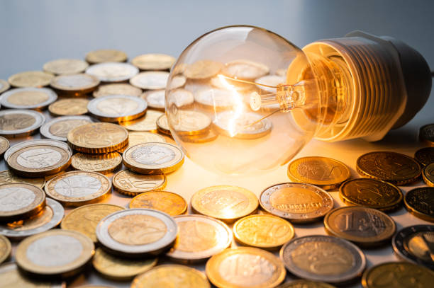 istock Light bulb turned on, with coins around. Energy costs. 1388968106