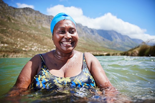 Portrait of a smiling mature African woman in a swimsuit and cap swimming in the ocean in the summertime