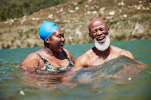 Mature African couple in swimwear laughing while swimming together in the ocean during a summer vacation