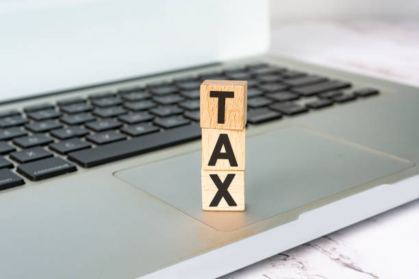 Tax text on wooden block cube placed on laptop or notebook. Tax concept. stock photo