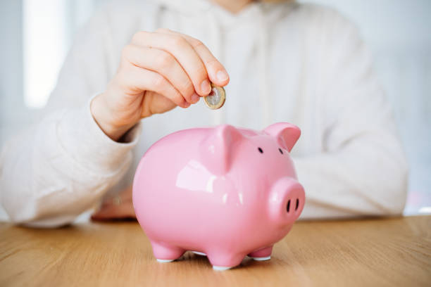 woman hand putting money coin into piggy for saving money - nota de pound britânico imagens e fotografias de stock