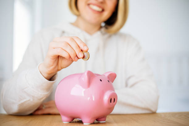 woman hand putting money coin into piggy for saving money - women savings uk coin imagens e fotografias de stock