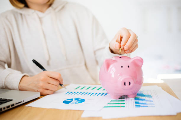 woman hand putting money coin into piggy for saving money - women savings uk coin imagens e fotografias de stock