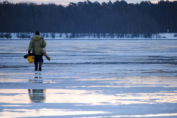 Angler on a frozen lake Lublin, Poland - February 2020: A lone angler on a frozen lake on a cloudy day man ice fishing stock pictures, royalty-free photos & images