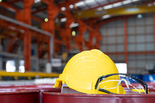Selective focus at safety hardhat that put on the heavy machine inside of the factory production line. Safety and protection gear concept in industrial area to prevent injury of worker or accident.
