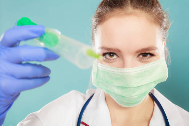 Medication and cure. Injection concept. Young woman doctor holding syringe. Female specialist with mask on face and vaccine in hand.