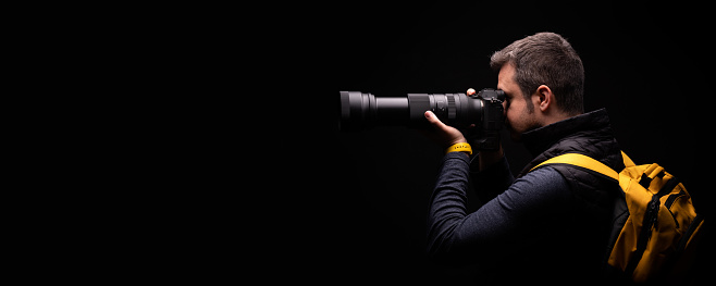 Portrait of a photographer with yellow bag taking a photo with a black background in studio