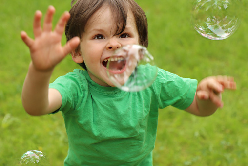 A little boy plays with soap bubbles in the summer outdoors.