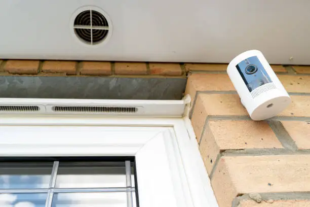 Newly installed, battery-powered wireless Internet-of-Things security camera installed near a ground floor kitchen window, under the eaves.
