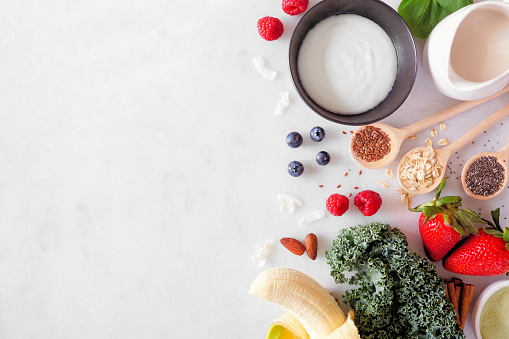 Healthy food side border. Smoothie making concept. Overhead view on a white marble background. Copy space. Fruit, yogurt, almond milk and a selection of ingredients.