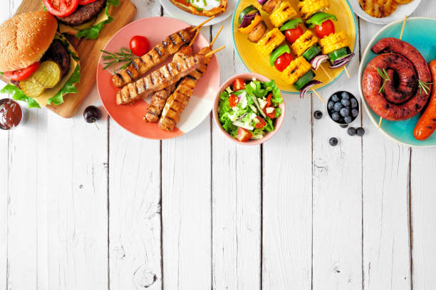 Summer BBQ or picnic food top border on a white wood background Summer BBQ or picnic food top border. Variety of burgers, grilled meat, vegetables, fruits, salad and potatoes. Overhead view on a white wood background. Copy space. food flat lay stock pictures, royalty-free photos & images