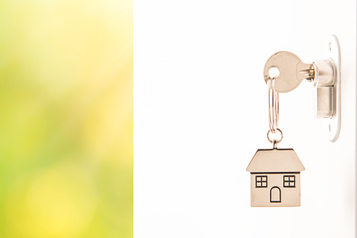 Woman using a house key on the front door. Close up of he womanâs hand. She is turning the key in the lock. Back lit. The key ring has a house icon on it.