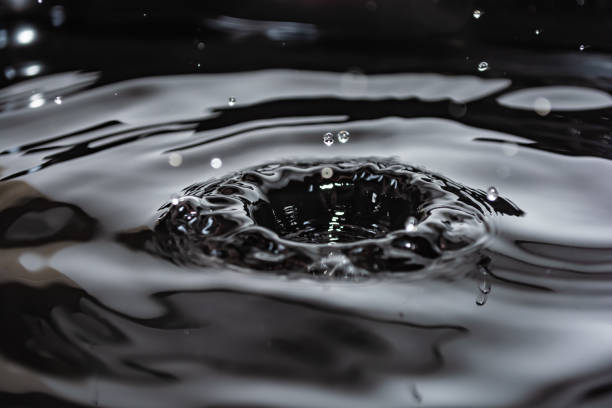 Splashes and waves from falling water drops on the surface of a liquid. Photo in black and white. Selective focus.
