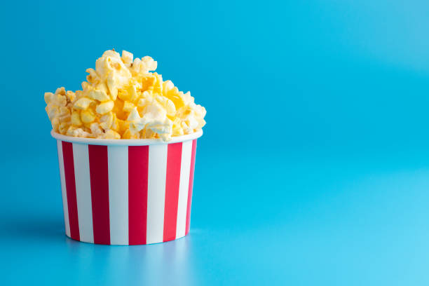 palomitas de maíz en un recipiente a rayas rojas y blancas sobre un fondo azul - palomitas fotografías e imágenes de stock