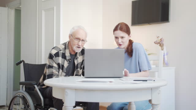 Woman explaining to her grandfather how to use a laptop
