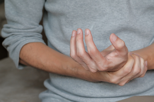 Asian man holding hand with muscle weakness, numbness and paralysis symptoms after vaccination. Guillain Barre syndrome rare cause by autoimmune disorder concept. Selective focus.