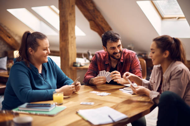 istock Young happy friends talking while playing with cards at college dorm. 1389009271