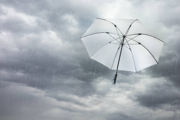 istock White umbrella blowing away in rainy storm sky. 1389010351