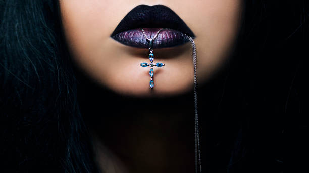 portrait d’une femme aux cheveux foncés aux lèvres foncées avec une croix dans la bouche - goth photos et images de collection