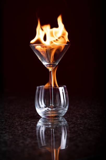 ein martini-glas in einem cognac-glas brennt beide mit fließenden gelben und orangefarbenen flammen - martini brand vermouth stock-fotos und bilder