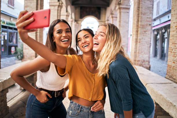 tres alegres amigas con ropa de verano tomándose una selfie al aire libre en el centro urbano turístico de la ciudad - child laughing blond hair three people fotografías e imágenes de stock