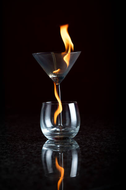 ein martini-glas in einem cognac-glas brennt beide mit fließenden gelben und orangefarbenen flammen - martini brand vermouth stock-fotos und bilder