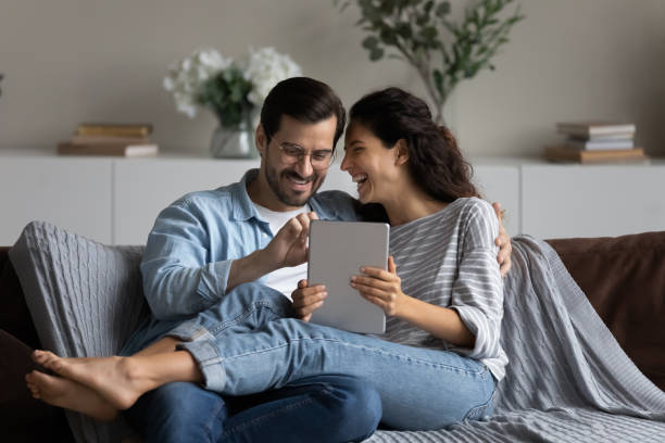 istock Happy laughing couple having fun with tablet at home together 1389029778