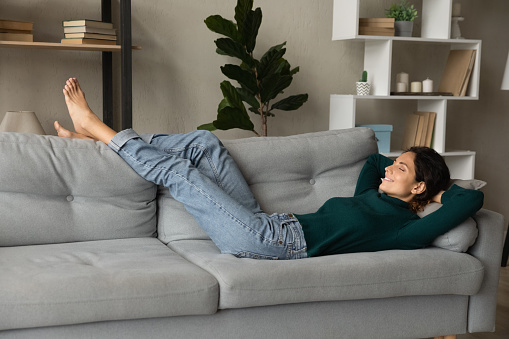 Peaceful hispanic woman relax rest on comfortable couch at home sleep or daydream with eyes closed. Calm Latino female renter lying on sofa in living room take nap relieve negative emotions.