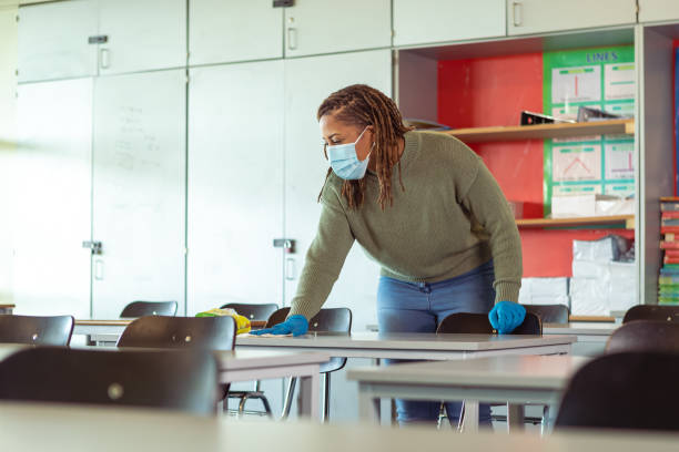 istock Female teacher wearing protective face mask cleaning classroom 1389037740
