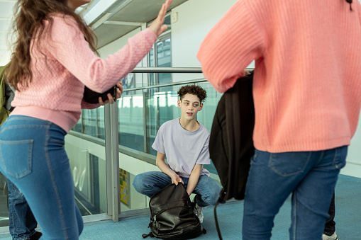 A tween boy talks with friends in the school hallway while getting homework out of his backpack before class starts.
