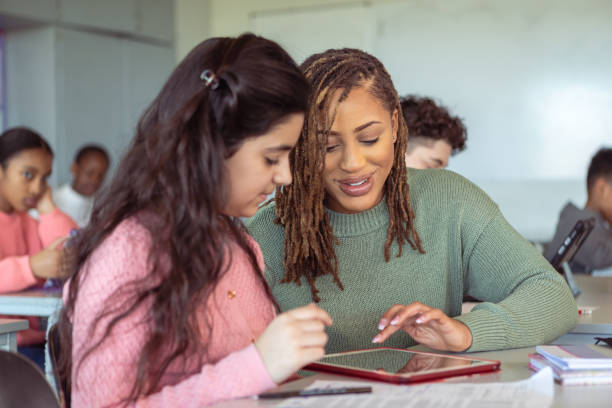 Teacher helping student with assignment on tablet computer stock photo