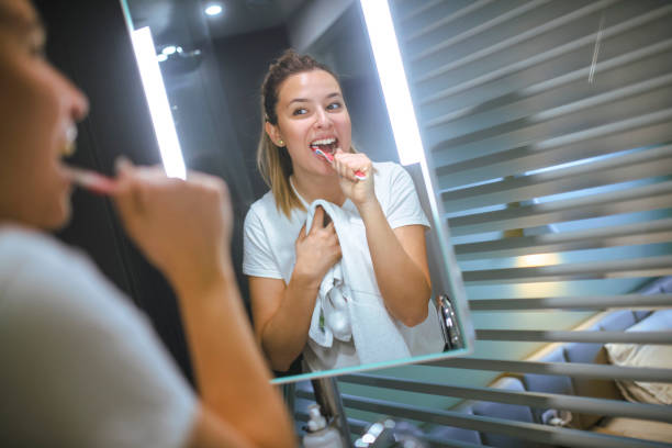 In a modern, lighted bathroom, a woman brushes her teeth and prepares for bed. Portrait of a beautiful woman brushing her teeth in the bathroom at home. brushing teeth stock pictures, royalty-free photos & images