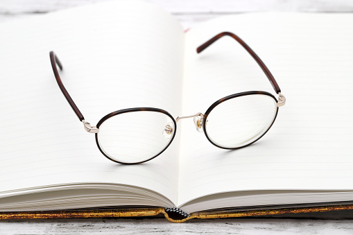 Stylish eyesight glasses and opened notebook on white wooden table