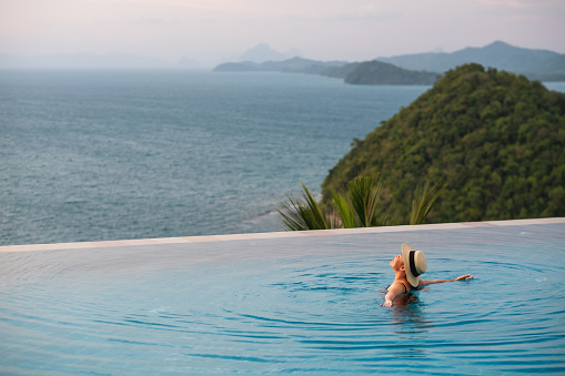 A young woman relaxing in infinity swimming pool with a beautiful sea view