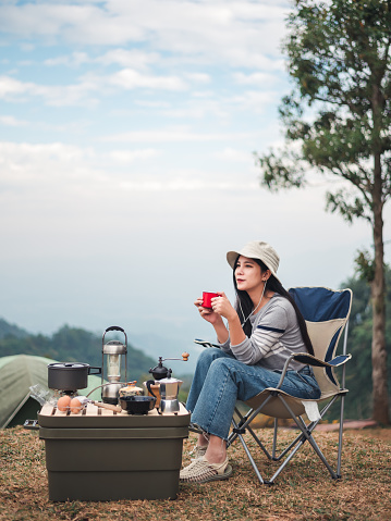 Hipster asian woman camper relaxing and enjoying camping alone ,drinking coffee in the morning