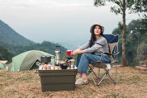 Hipster asian woman camper relaxing and enjoying camping alone ,drinking coffee in the morning